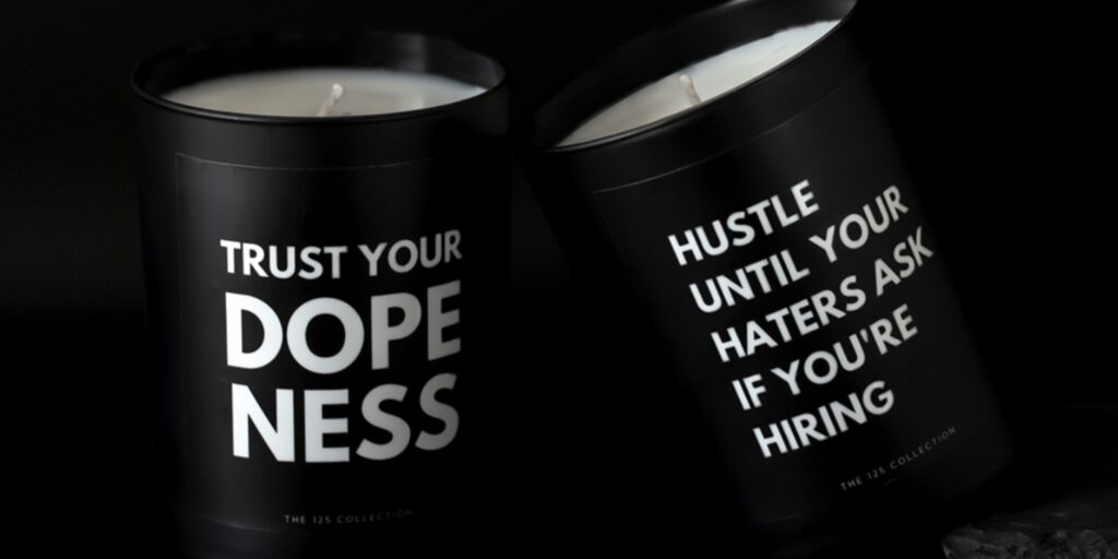 Candles from The 125 Collection that say "Trust Your Dopeness" and "Hustle Until Your Haters Ask If You're Hiring