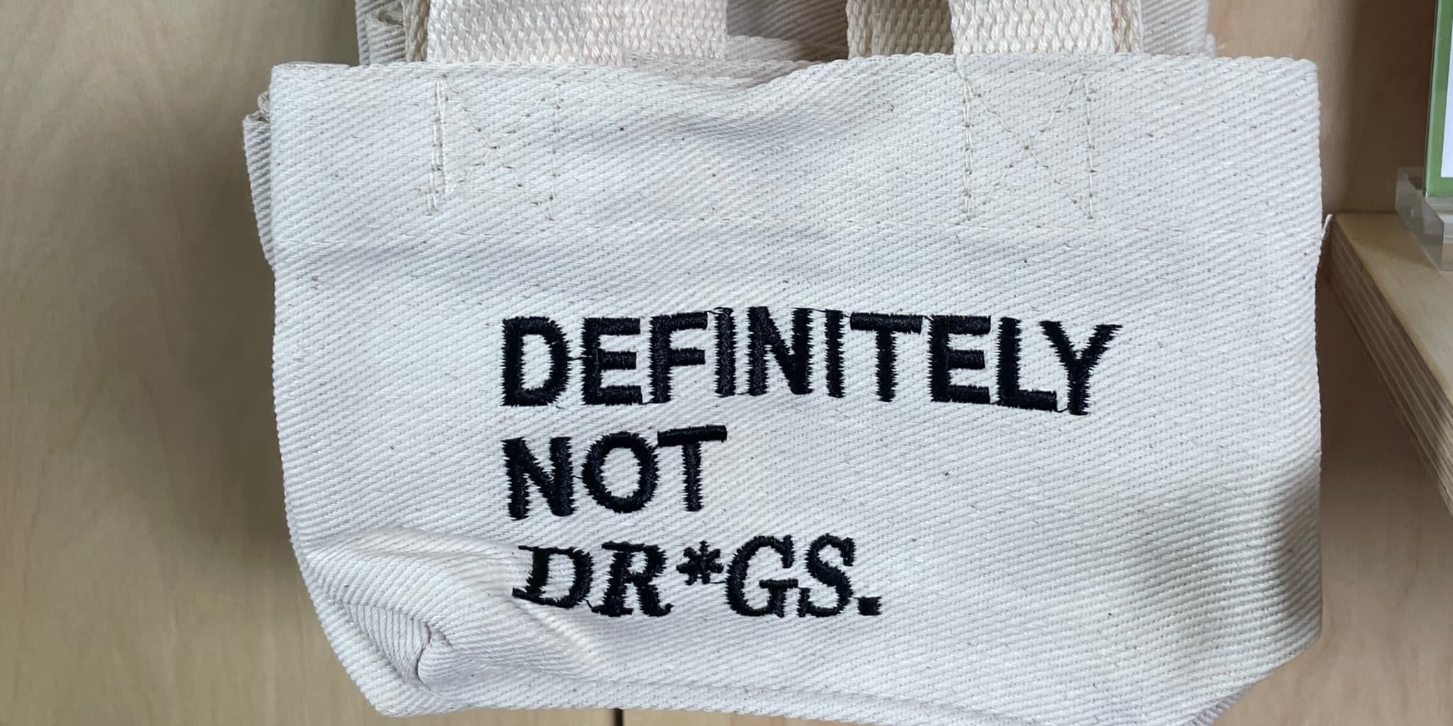 A canvas tote bag that reads "Definitely Not Dr*gs"