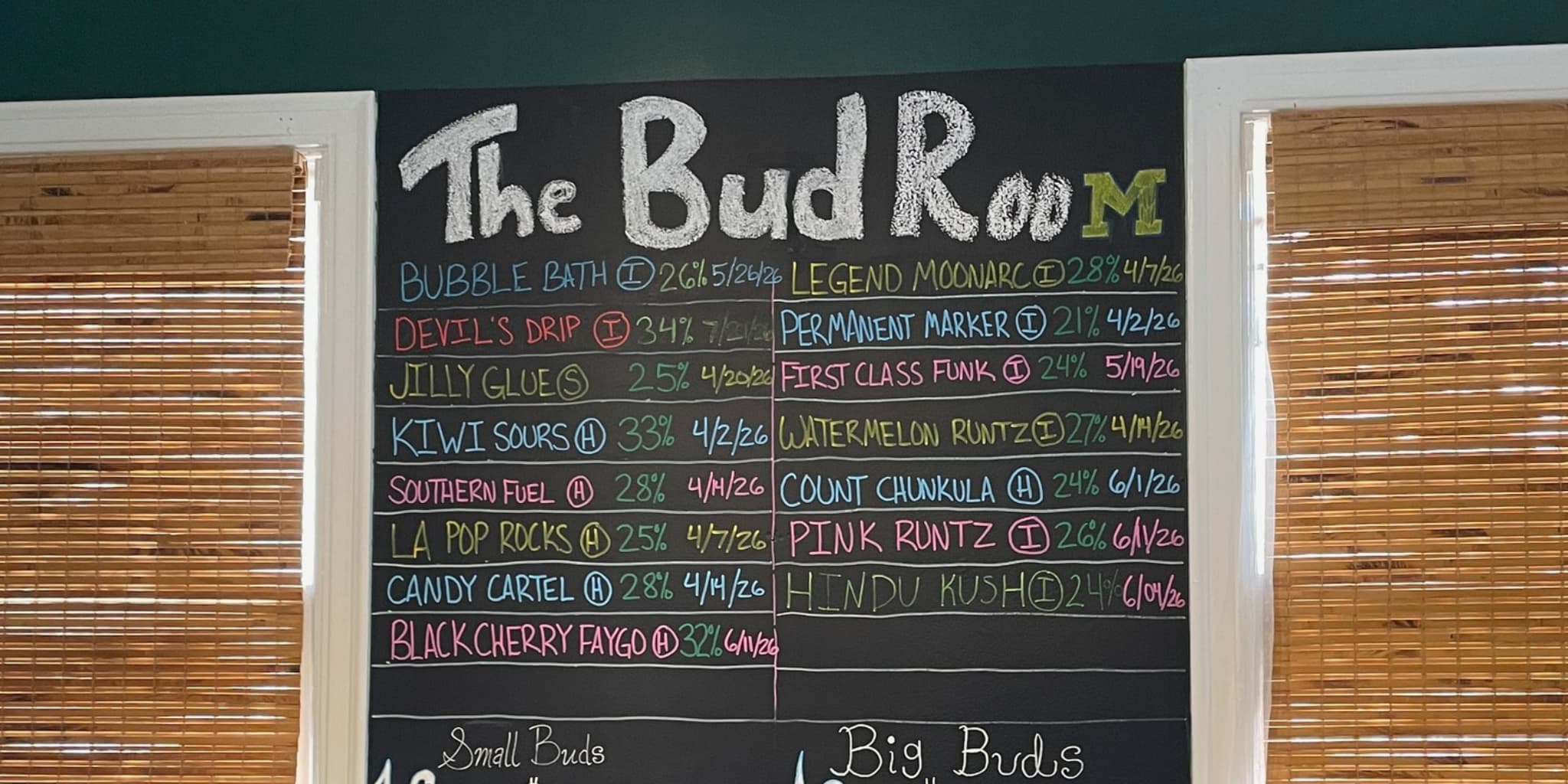 A chalkboard sign reading The Bud Room with several cannabis strains listed for sale.