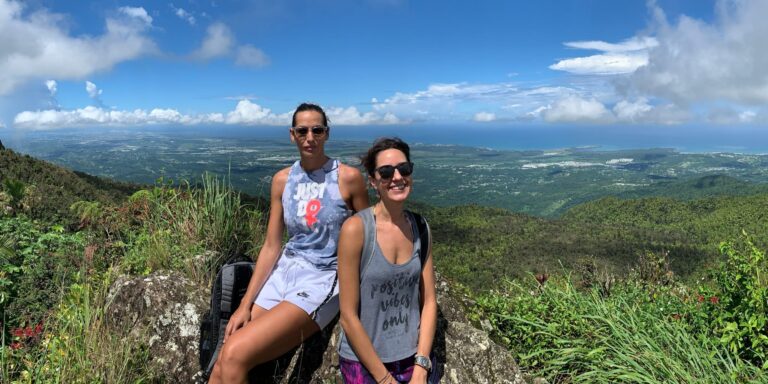 Two women posing on top of a mountain with the sky in the background