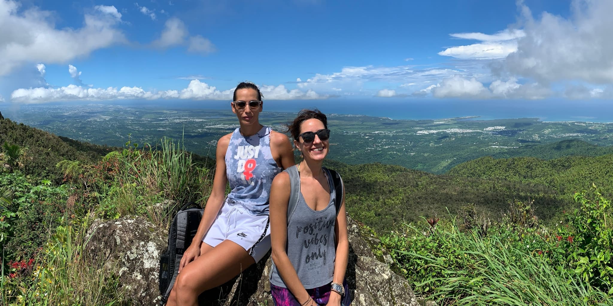 Two women posing on top of a mountain with the sky in the background